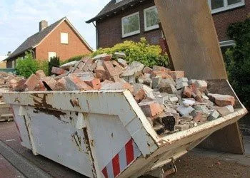 A white skip filled with red bricks and rubble in a residential area