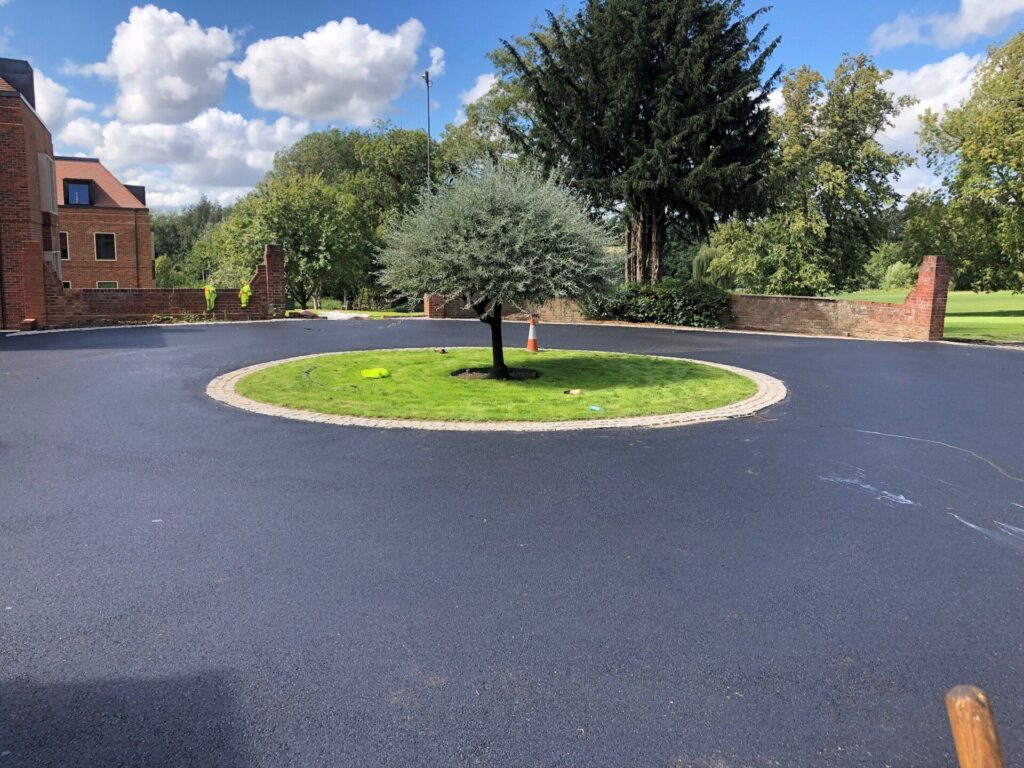 Newly resurfaced driveway with a circular grass island and tree in the very centre.