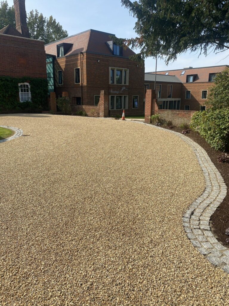 A driveway that has recently been treated with surface dressing by Hazell & Jefferies, leading up to a large red brick building.