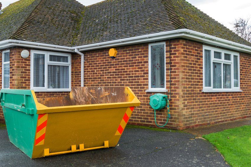 An empty yellow skip next to a red brick house