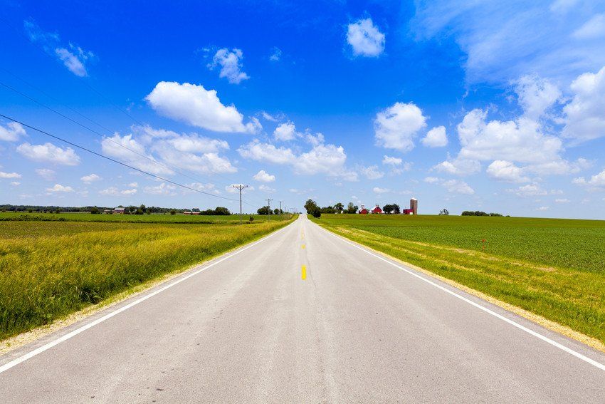 Long view of a road stretching ahead between green grass.