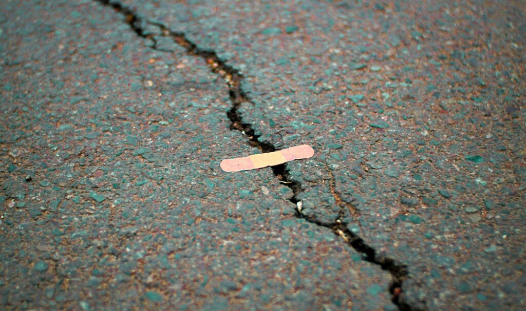 A long crack in a road surface with a medical plaster on it.