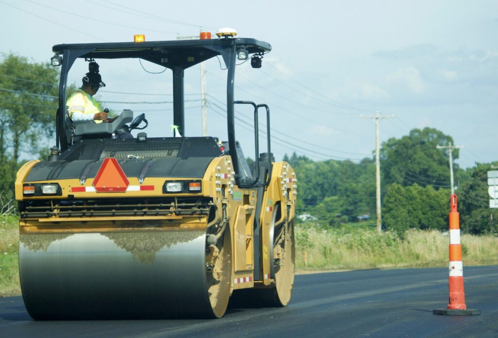 A steam roller travelling down a wide, open road.