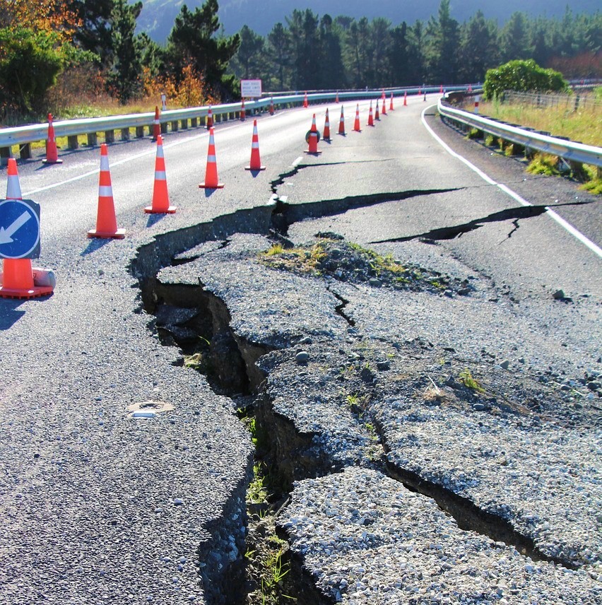 Large cracks in a stretch of road, cordoned off with traffic cones.